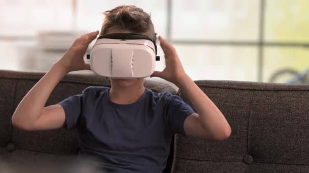 Мальчик снимает наушники виртуальной реальности на диване — стоковое видео