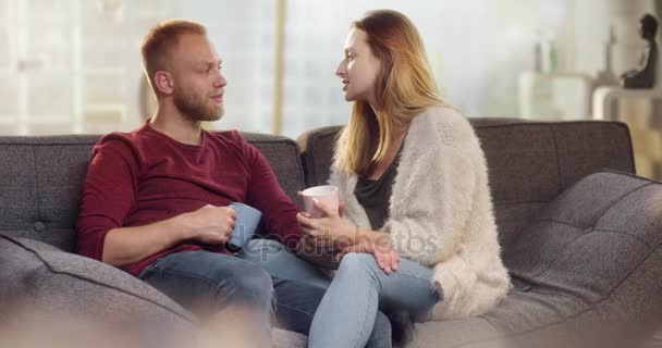 Doce jovem casal discutindo coisas no sofá enquanto bebe chá — Vídeo de Stock