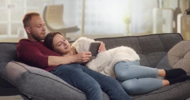 抱きしめるとタブレットの面白いものを見てソファの上にクールなカップル — ストック動画
