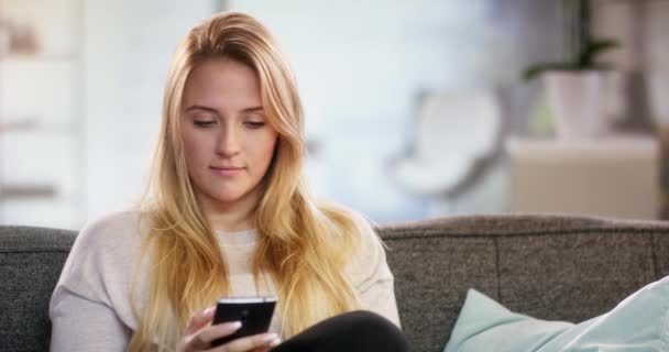 Jovem mulher atraente sentado em casa e usando smartphone — Vídeo de Stock