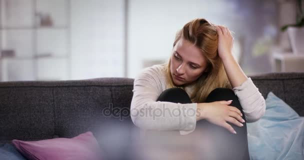 Sorgsen ung kvinna sitter i soffan håller armarna framför henne — Stockvideo
