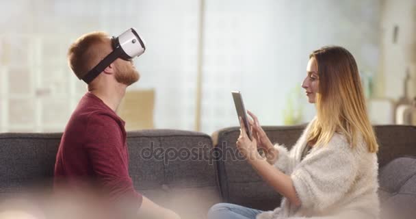 Vr のヘッドセットとタブレットで遊んでのソファの上の甘いカップル — ストック動画