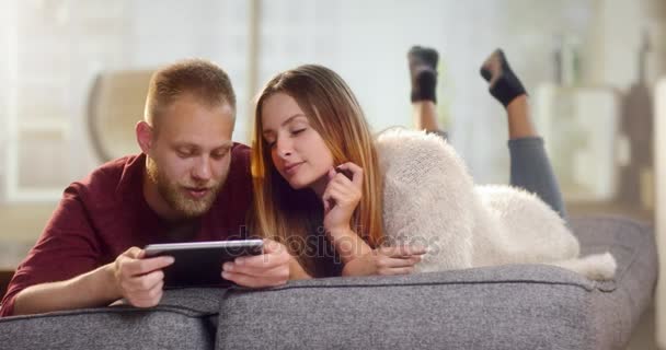 Jeune couple doux couché sur un canapé et commander quelque chose sur une tablette — Video