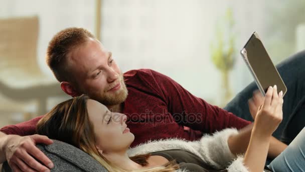 Jovem casal alegre no sofá casa usando um tablet — Vídeo de Stock