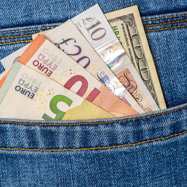 Closeup of various countries banknotes peeking out of blue jeans — Stock Photo, Image