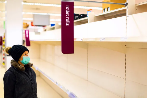 保護医療マスクを着用しているシニア女性の顧客は スーパーマーケットでのトイレットペーパーのロールの空の棚で混乱しているように見えます Covid 19パンデミックコロナウイルス ストック写真