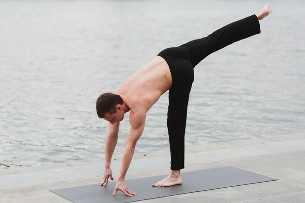 A young man practicing yoga asanas in the city on the waterfront — Stock Photo, Image