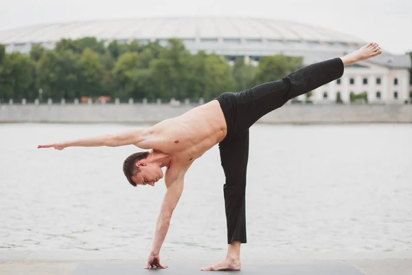 A young man practicing yoga asanas in the city on the waterfront — Stock Photo, Image