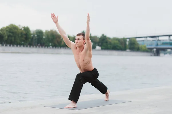 En ung man öva yoga asanas i staden vid vattnet — Stockfoto