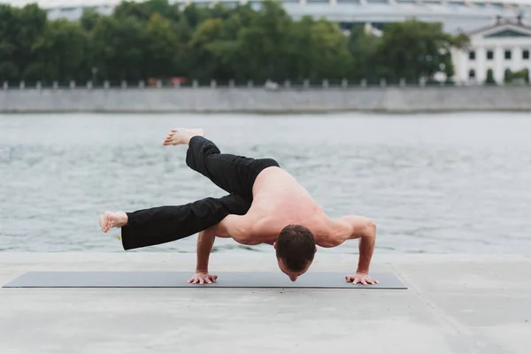 En ung man öva yoga asanas i staden vid vattnet — Stockfoto