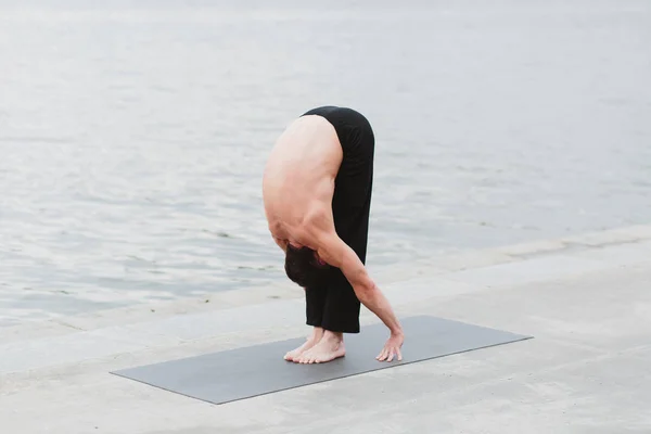 En ung man öva yoga asanas i staden vid vattnet — Stockfoto