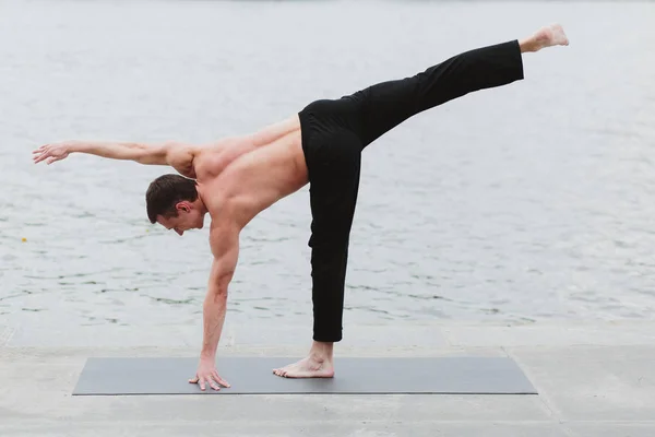 En ung man öva yoga asanas i staden vid vattnet — Stockfoto