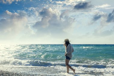 Young woman in a hat walking along the seashore. Holidays and tr clipart