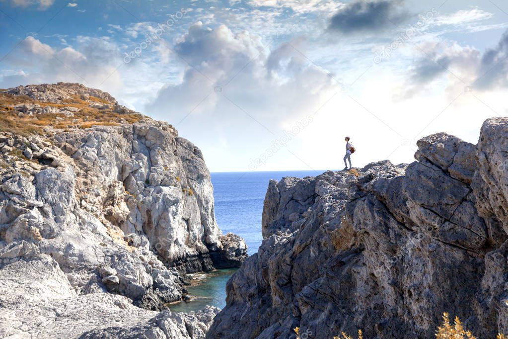 Young woman tourist is standing on a high cliff overlooking the 