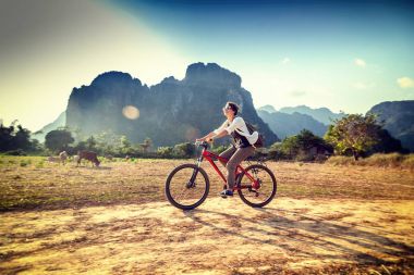 Happy tourist woman riding a bicycle in mountain area in Laos. T clipart