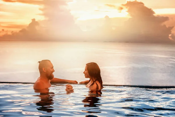 Casal romântico na piscina infinito ao pôr do sol com vista para o s — Fotografia de Stock
