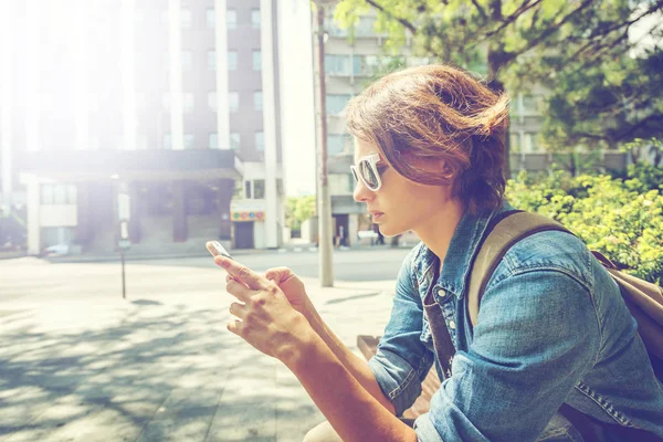 Młoda kobieta z telefonu komórkowego w rękę na ulicy tle — Zdjęcie stockowe