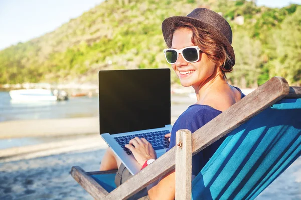 Счастливая молодая женщина с ноутбуком работает на пляже на солнце. Ж — стоковое фото