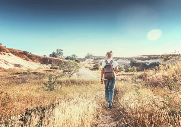 Dziewczynka z plecakiem spacery po polu w promieniach brukowana — Zdjęcie stockowe