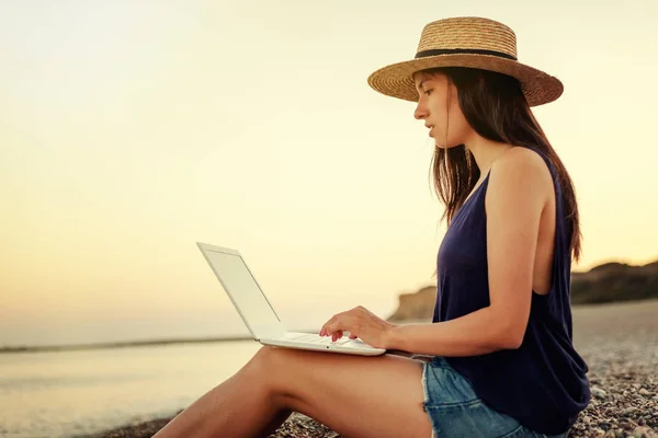 Mooie jongedame in een hoed en shorts met een laptop zitten — Stockfoto