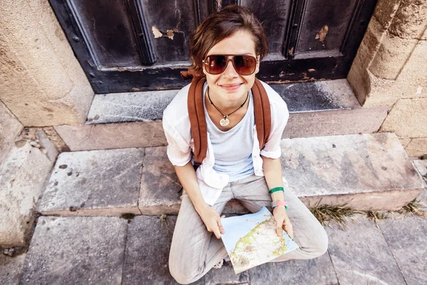 Young woman tourist with a card in her hands sits on the steps i — Stock Photo, Image