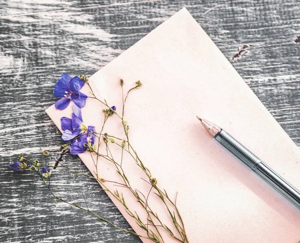 Folha de caneta de papel e flor de campo seco em uma mesa de madeira — Fotografia de Stock