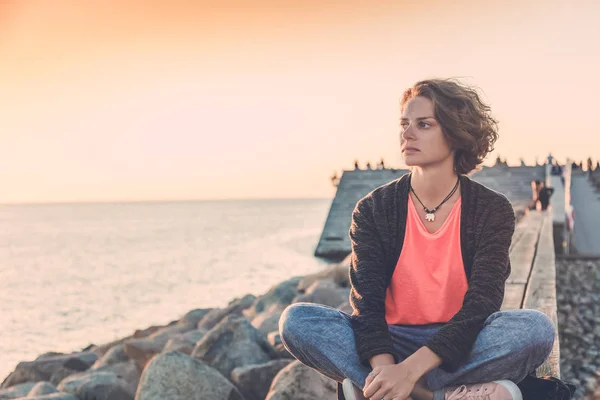 Молодая женщина, сидящая на пляже и наблюдающая за закатом — стоковое фото