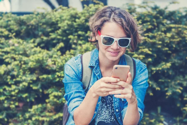 Mladá žena s mobilním telefonem v ruce na ulici pozadí — Stock fotografie