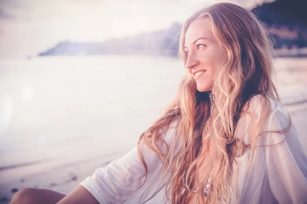 Hermosa joven con el pelo largo y rubio sentado en la playa — Foto de Stock