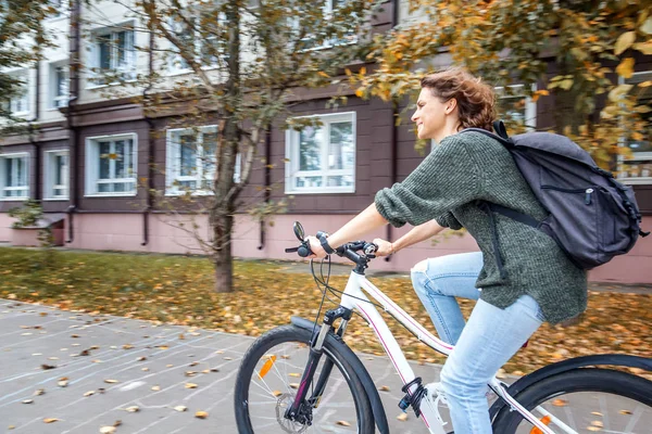 Mooie jonge vrouwelijke student in een trui en jeans op een bicyc — Stockfoto