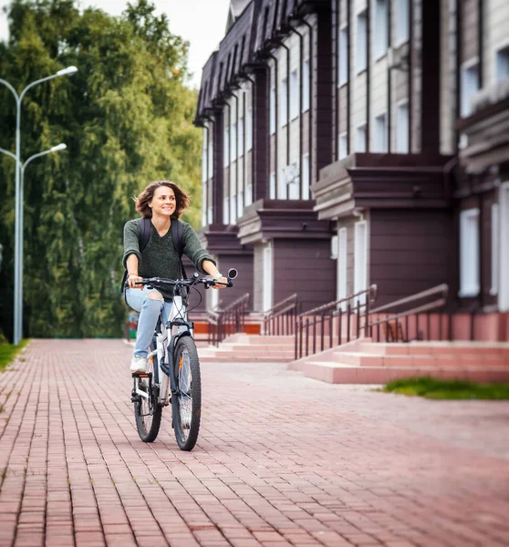 Beautiful young female student in a sweater and jeans on a bicyc — Stock Photo, Image