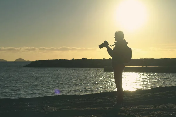 Silhouet van een jonge vrouw met een camera in de hand op een zonsondergang ba — Stockfoto