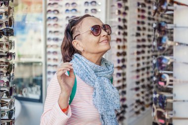 Güzel, şık, yaşlı bir kadın güneş gözlüğü bir optik seçer.