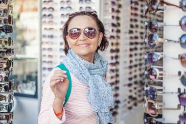 Güzel, şık, yaşlı bir kadın güneş gözlüğü bir optik seçer.