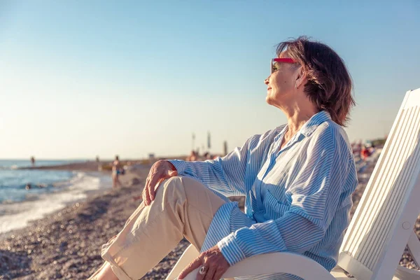 Красивая пожилая женщина, сидящая в шезлонге на пляже и — стоковое фото