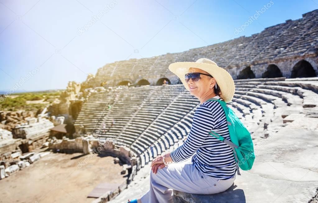 Mature beautiful woman traveler, sits on the steps of the amphit