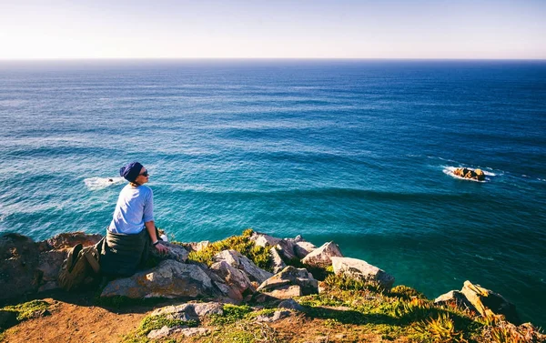 Joven hermosa mujer se sienta en una piedra en el fondo de Cabo — Foto de Stock