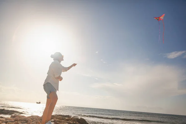 Mooie gelukkig jonge vrouw meisje lanceert een vlieger op de kust — Stockfoto