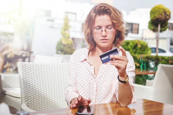 Menina atraente nova em óculos com um cartão de crédito e um telefone — Fotografia de Stock