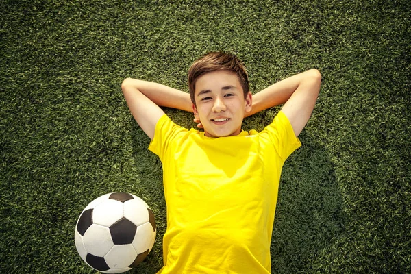 Adolescente feliz con una pelota de fútbol acostado en el césped verde. Sh. — Foto de Stock