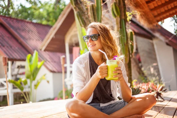 Kaunis nuori nainen istuu kahvilassa tropiikissa ja juo — kuvapankkivalokuva