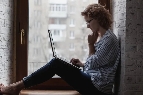 Atraktivní mladá žena sedí na okně s přenosným počítačem, freelan — Stock fotografie