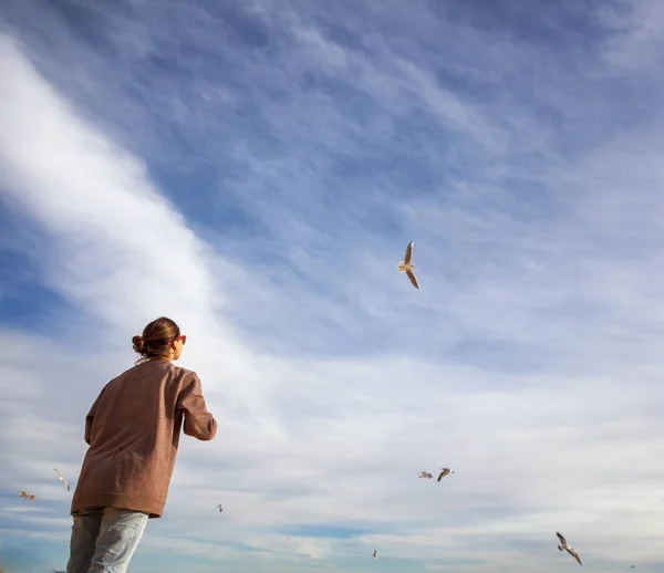 Una chica mira al cielo con nubes y observa gaviotas voladoras — Foto de Stock