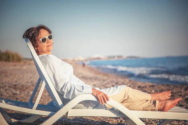 Bela mulher idosa sentada em uma cadeira de praia e — Fotografia de Stock