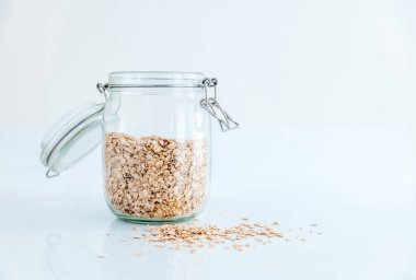Beyaz bir arka plan, sağlıklı cam bir kavanoza yulaf ezmesi yemek 
