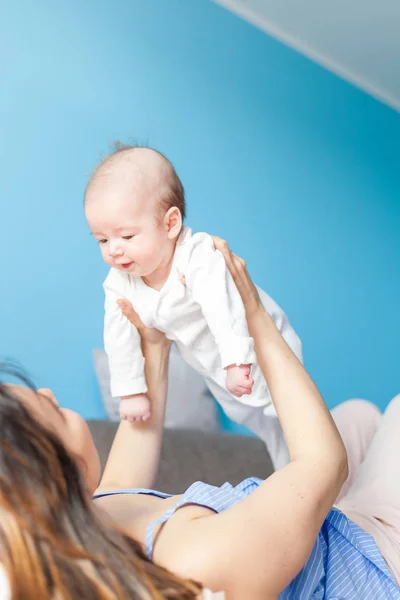 Schöne junge glückliche Frau spielt mit ihrem neugeborenen Baby liegt auf t — Stockfoto