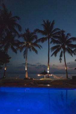 Günbatımı ve aydınlık yüzme havuzu, tropikal bir tatil köyünde.