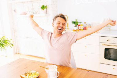 Mutfakta sütle kahvaltı eden mutlu genç sarışın adam. 