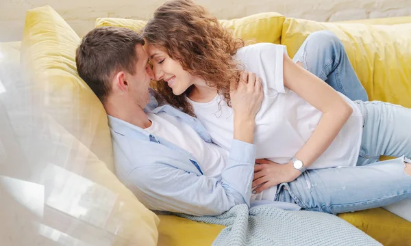 Young happy couple lying and hugging on the yellow couch in the — Stock Photo, Image