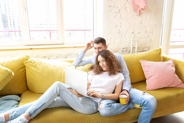 Молода щаслива пара лежить на жовтому дивані з ноутбуком в їх — стокове фото
